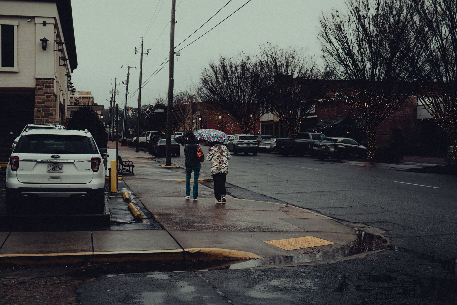 A moody, rainy street scene in downtown Canton, Georgia, featuring pedestrians with umbrellas.