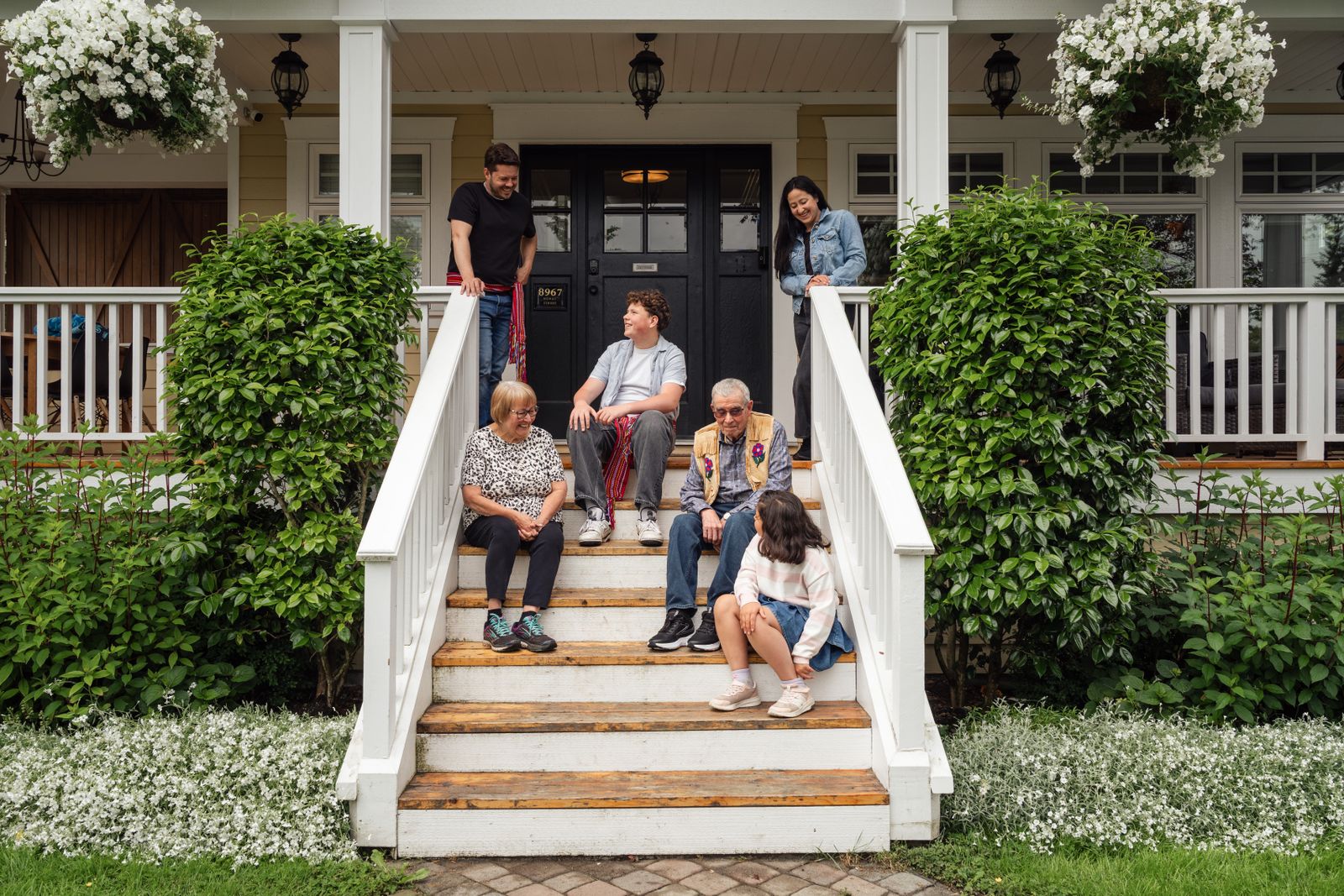 Multigenerational family enjoying a moment on porch steps surrounded by greenery.