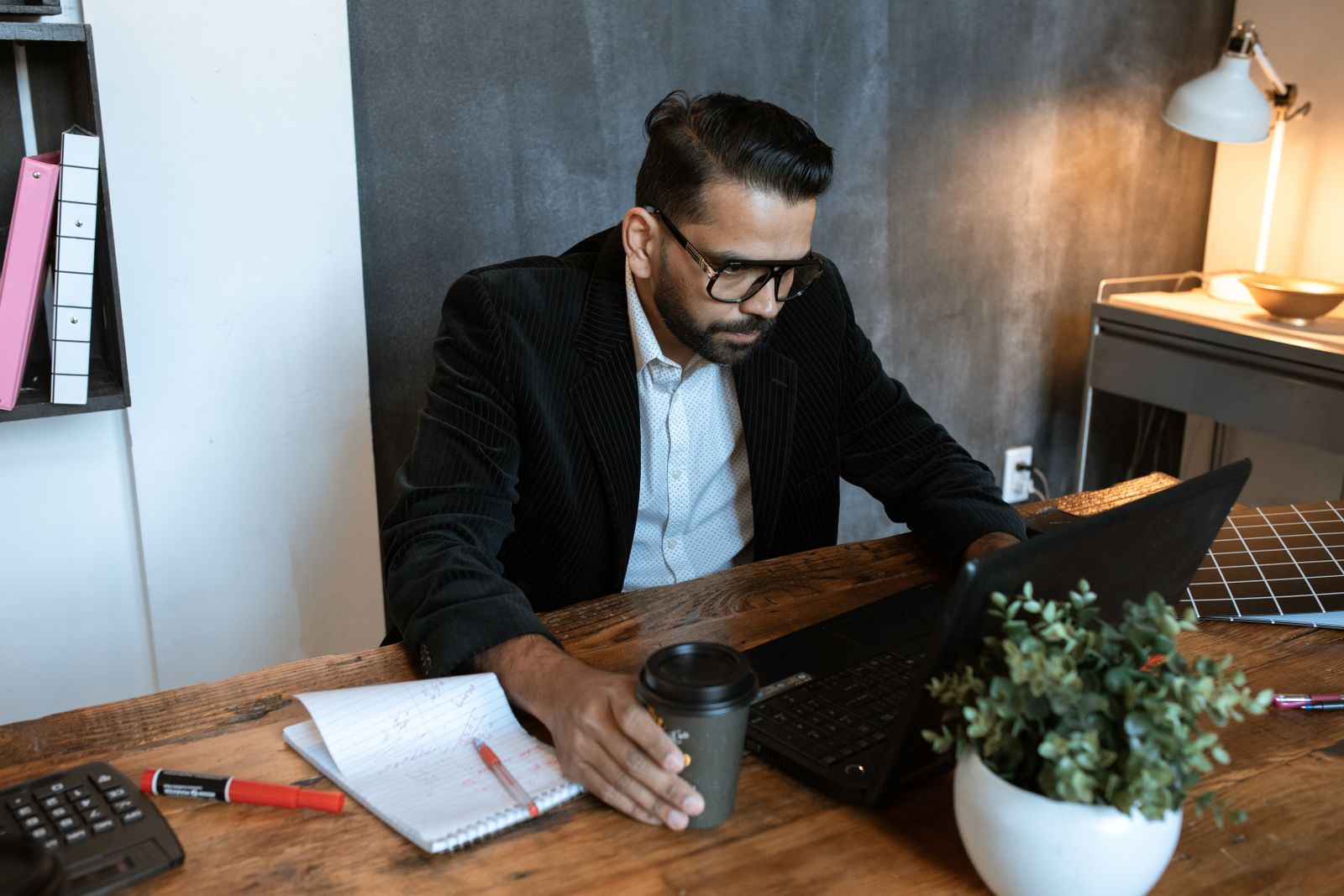 Man concentrating on laptop in a modern home office setting, coffee in hand.